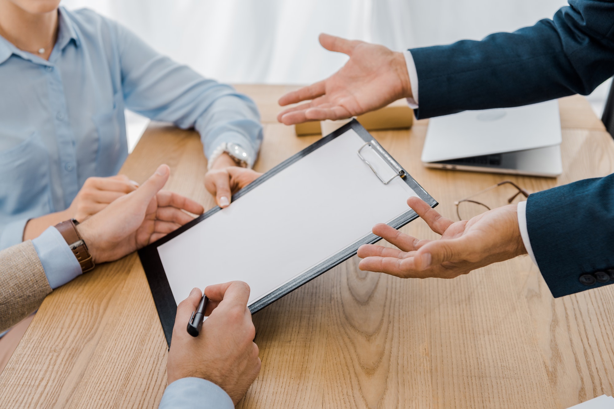 couple-signing-contract-on-clipboard-with-insurance-agent-at-wooden-table.jpg